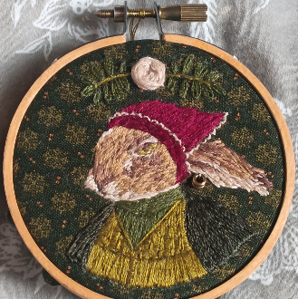 2024 handsewn embroidery hoop. a thread-painted hare wearing a red bandanna on its head and a green dress.